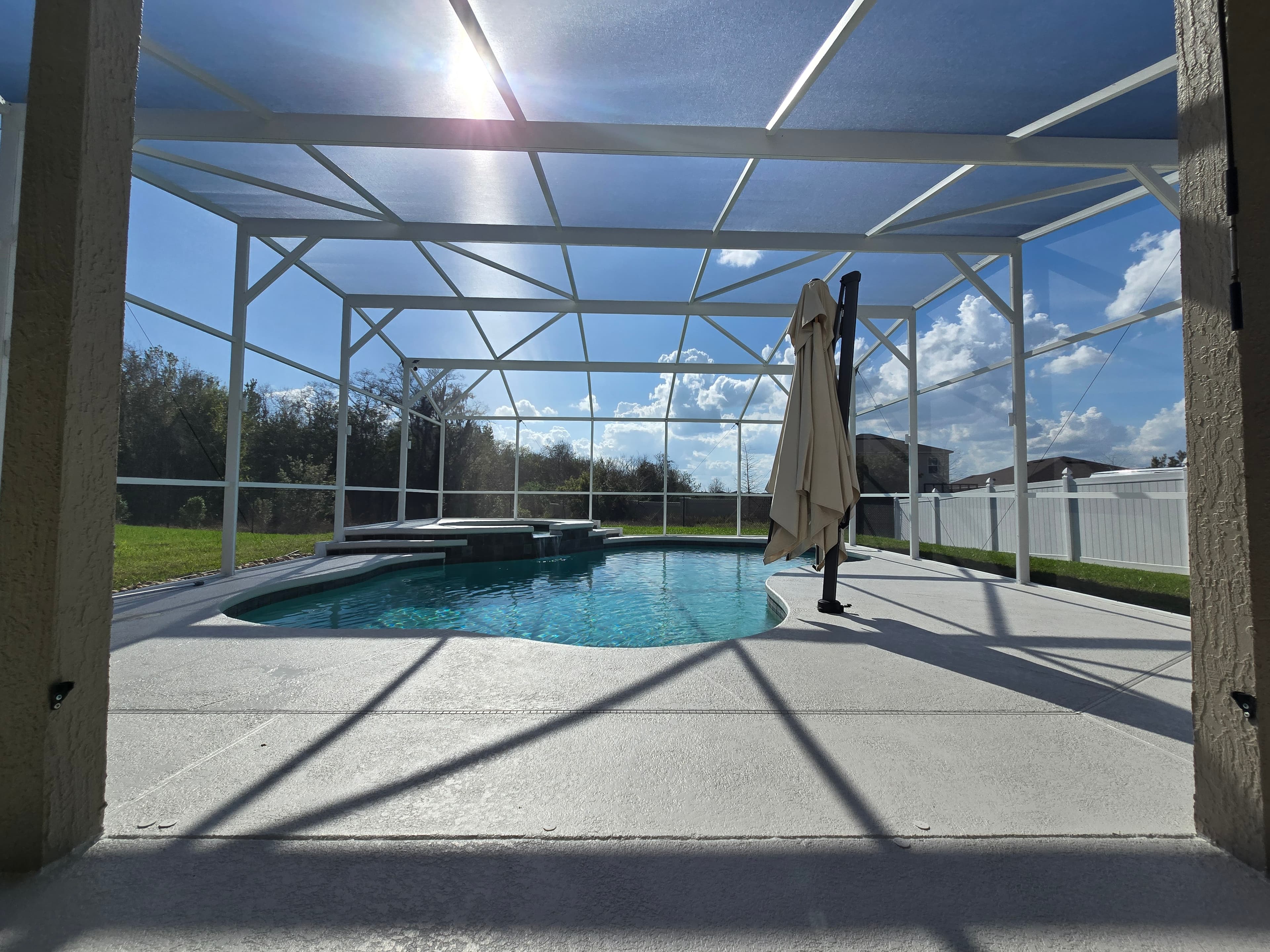 Sunny backyard swimming pool inside a white screen enclosure with a closed patio umbrella.