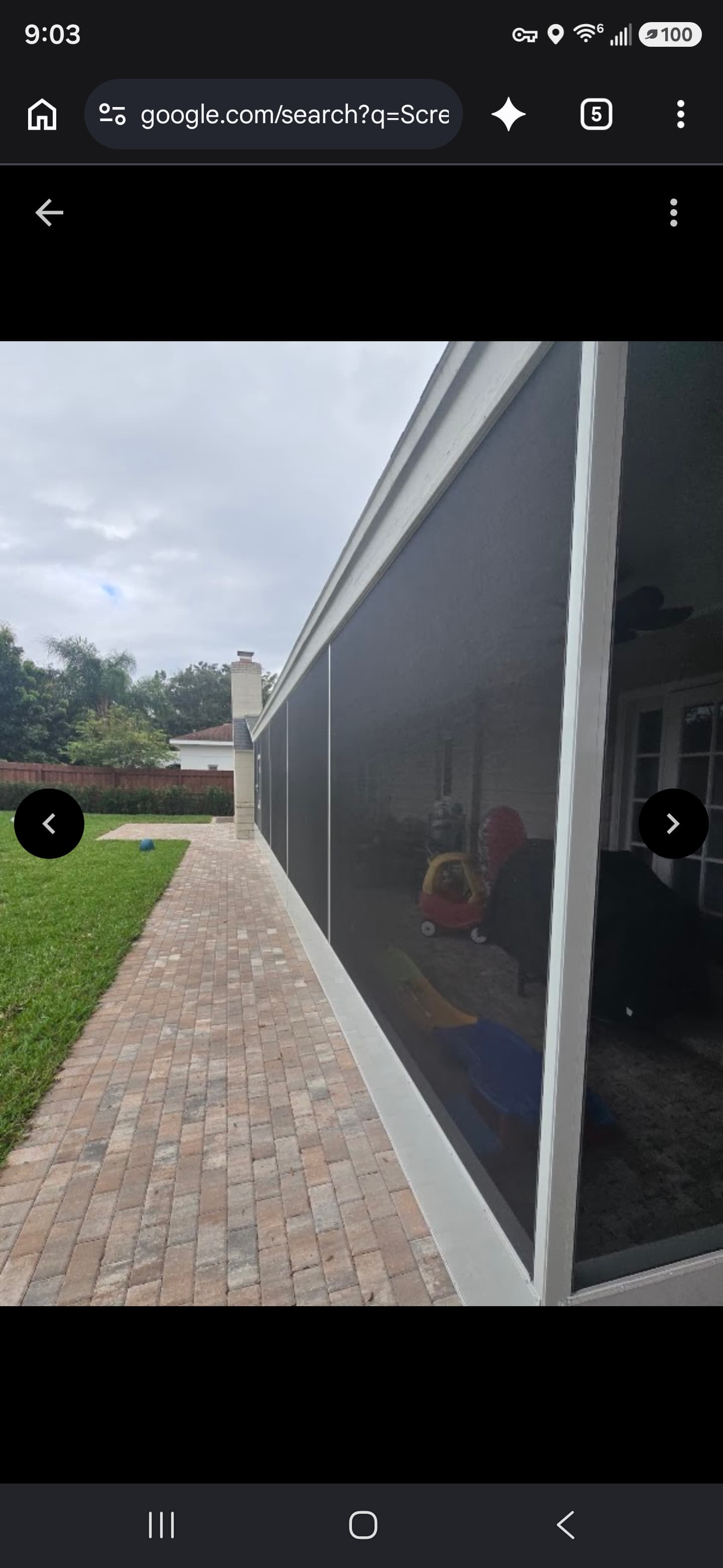 White screened-in patio enclosure next to a brick paver walkway and green lawn.