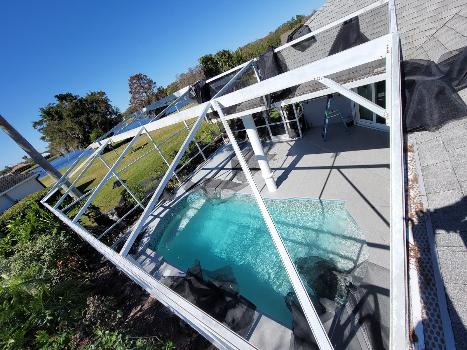 Torn black screen mesh hangs from a white metal frame over a blue pool.