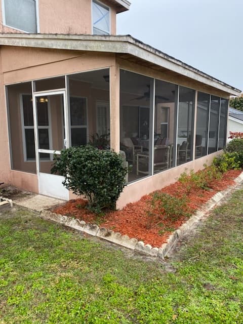 Screened-in porch with patio furniture and red mulch landscaping on a peach-colored house.